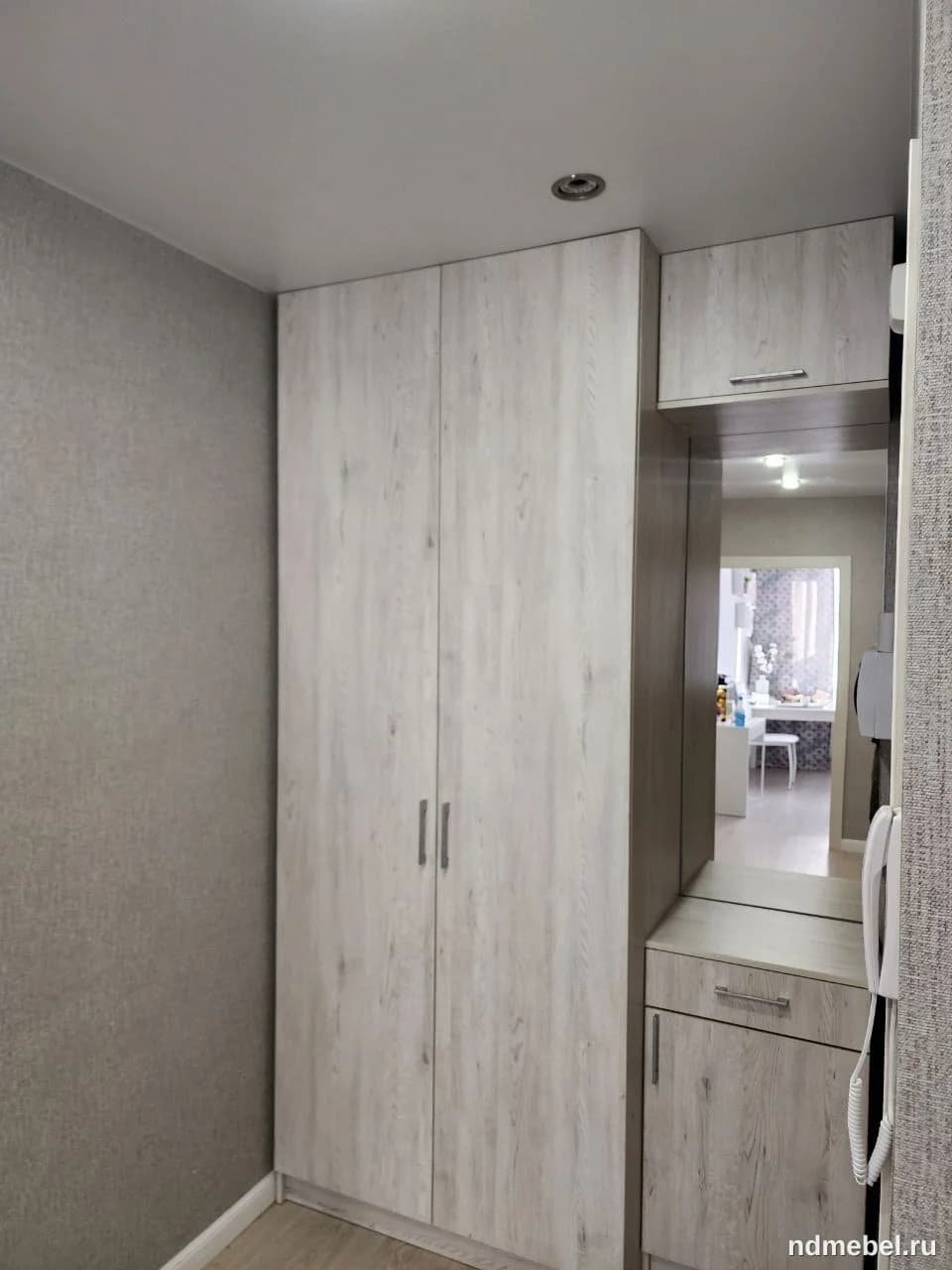Встроенный или корпусный шкаф-купе/система хранения в прихожей, выполненный из ЛДСП с имитацией светлого, выбеленного дерева. Мебель выполнена в современном минималистичном стиле и дополнена зеркальной вставкой и небольшой тумбой с ящиком.