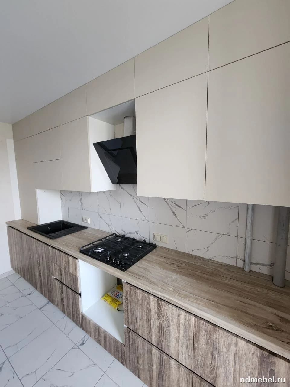 Современная кухонная мебель с гладкими верхними фасадами кремового/светло-бежевого цвета и нижними фасадами с текстурой натурального дерева (под дуб или орех). Композиция выполнена в минималистичном стиле с интегрированной черной вытяжкой.