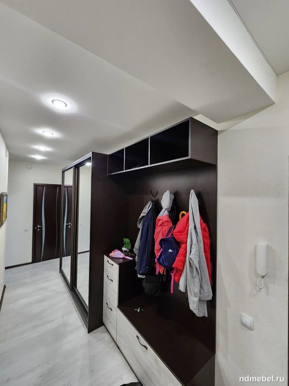 Это прихожая зона с современным мебельным гарнитуром, выполненным из материалов под темное дерево (венге) и светлое дерево/под бетон для ящиков. Мебель представляет собой комбинацию шкафа-купе с зеркальной дверью и открытой секции для верхней одежды с полками и банкеткой.