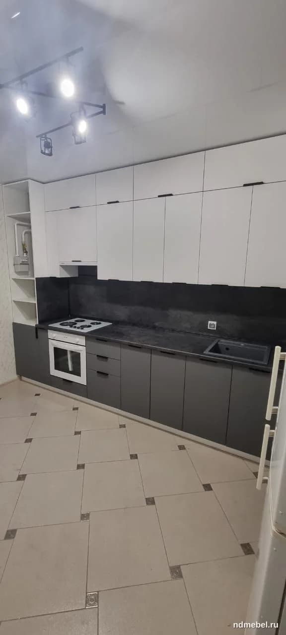 Современный кухонный гарнитур с матовыми фасадами в контрастном двухцветном исполнении: верхние шкафы белые, нижние — темно-серые или антрацитовые. Мебель выполнена в минималистичном стиле с интегрированными черными ручками и темной столешницей.