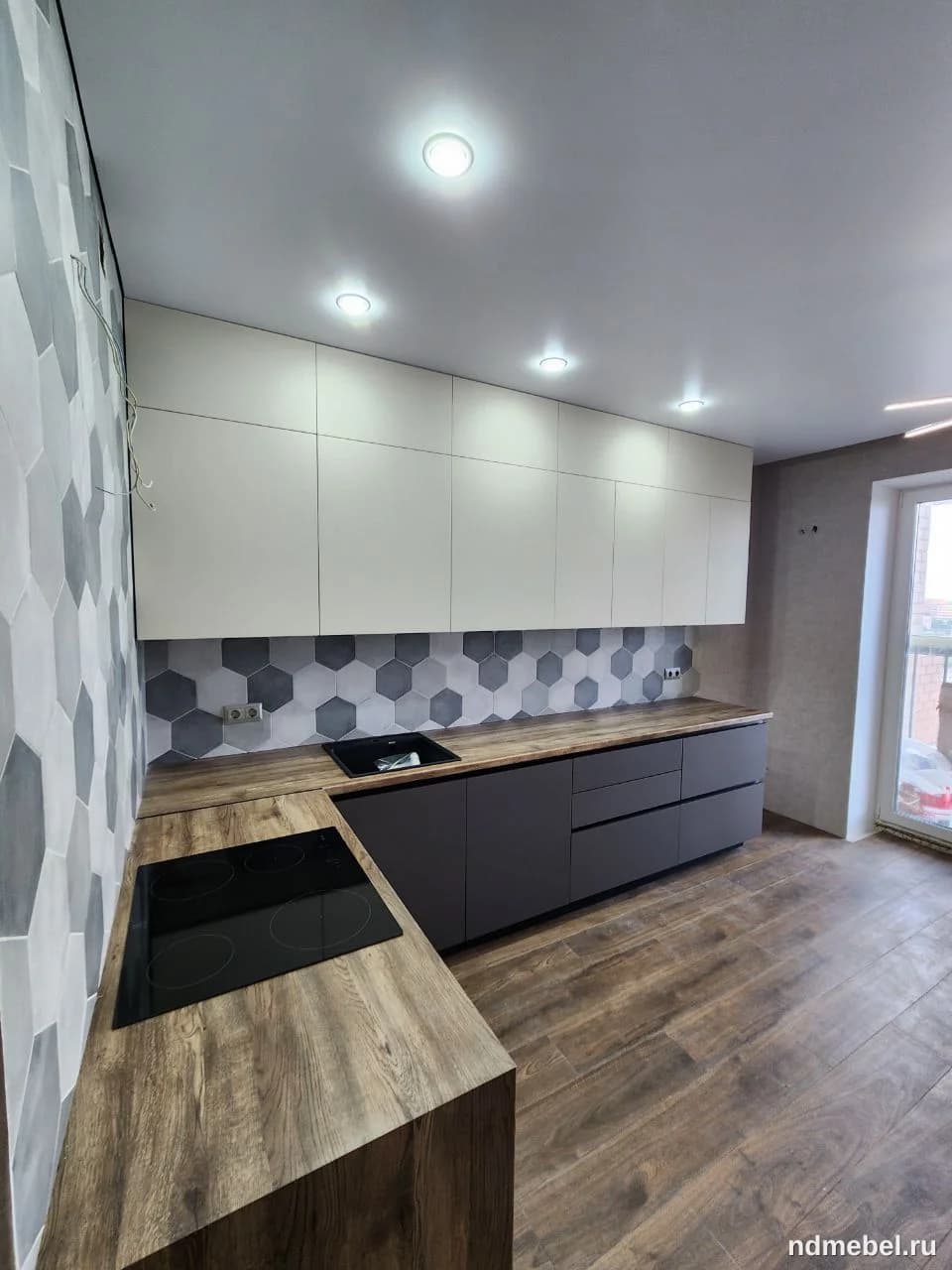 Современный линейный кухонный гарнитур с гладкими фасадами, сочетающий темный матовый низ и светлый верх, с контрастными столешницами под натуральное дерево. Дизайн выполнен в минималистичном стиле с акцентным фартуком из шестиугольной (гексагональной) плитки.
